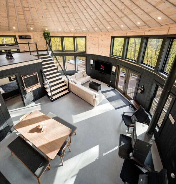 Un interior moderno con techo de madera, ventanas amplias, una escalera, una zona de estar y un televisor.