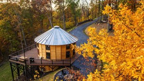 Una cabaña de madera con techo de metal, rodeada de follaje otoñal y una terraza con mobiliario exterior.