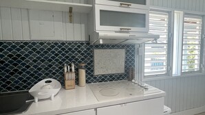 A kitchen with white cabinets, a white countertop, a backsplash with blue and white tiles, a microwave, and a window with blinds.