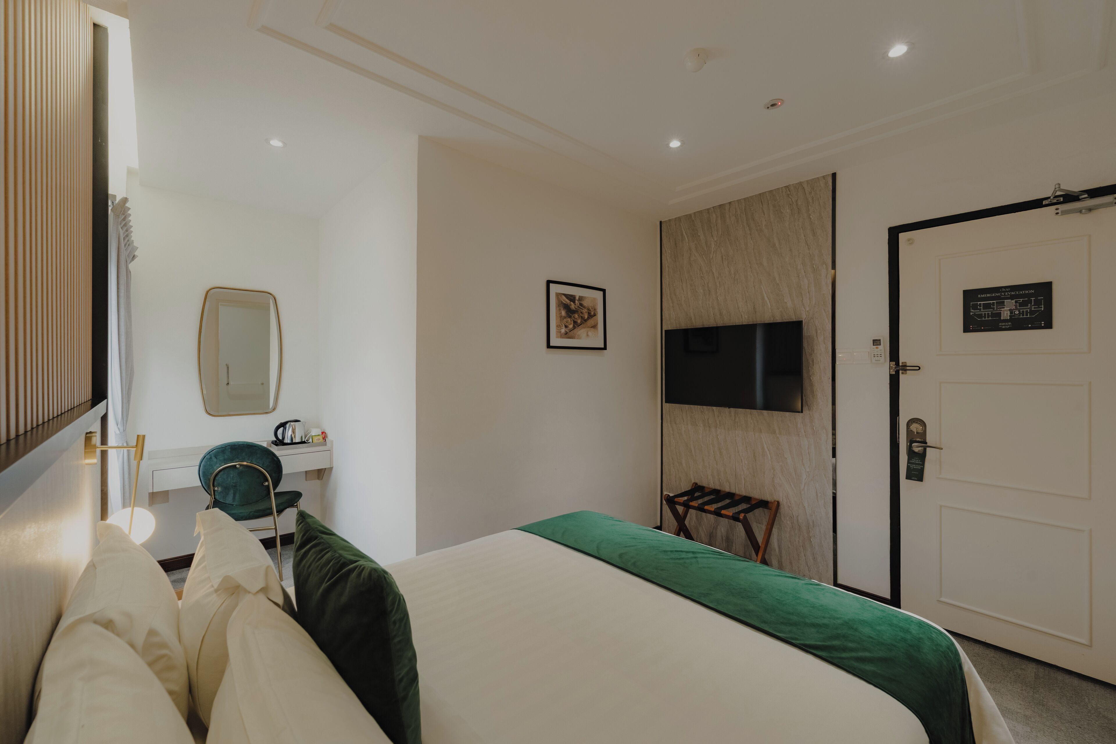 A hotel room with a bed, a desk with a chair, a television mounted on the wall, and a door with a lock.