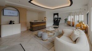 Een moderne hotellobby met een receptiebalie, zithoek en grote ramen.