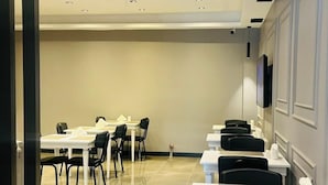 Un salón de conferencias con mesas y sillas blancas, un televisor de pantalla plana en la pared e iluminación empotrada en el techo.