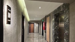 Un pasillo de hotel moderno con suelo de mármol, una puerta de madera y un ascensor.