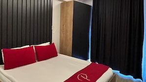 Una habitación de hotel moderna con una cama grande, almohadas rojas, un cabecero de madera y una manta roja.