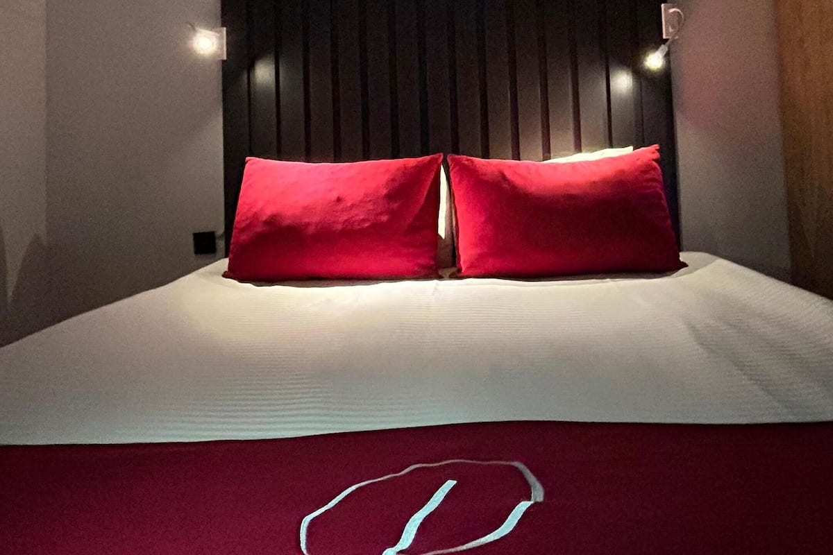 Una habitación de hotel con una cama grande, dos almohadas rojas, un cabecero oscuro y dos lámparas de noche.