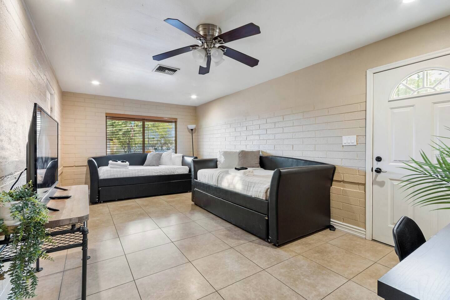 Une pièce moderne avec un ventilateur de plafond, deux canapés noirs, un téléviseur et une porte.