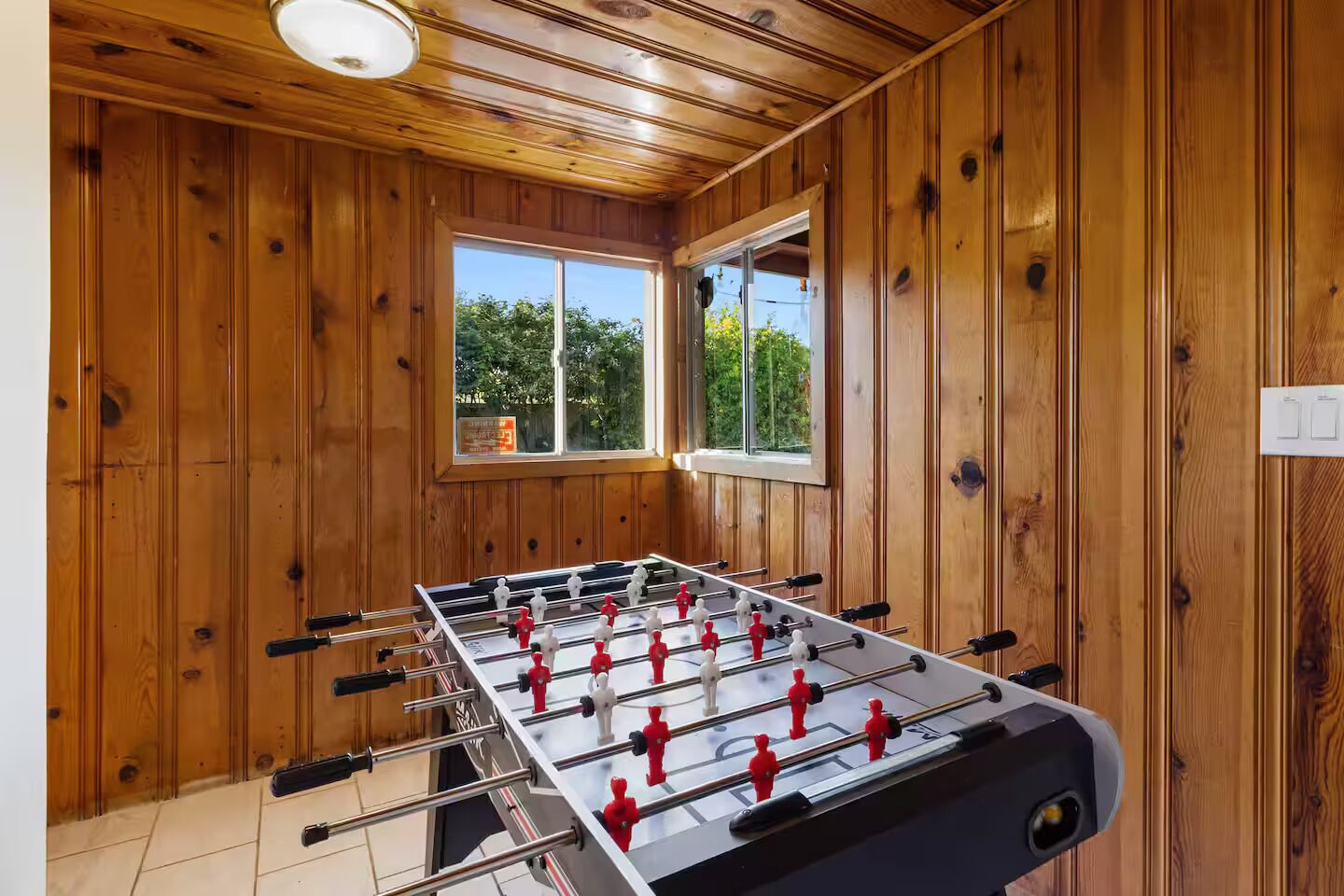 A wooden-floored room with a foosball table, a window, and a door.