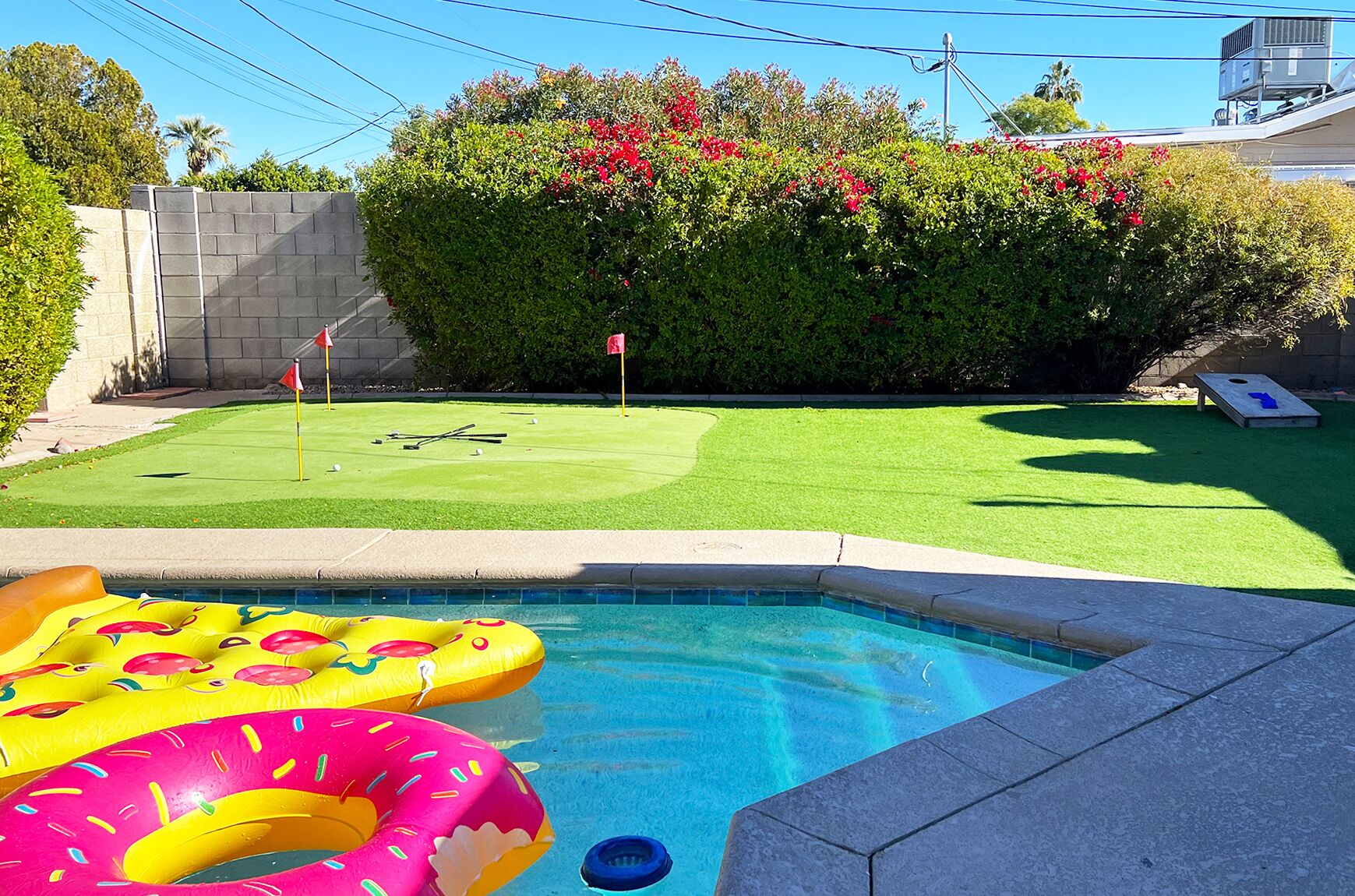 Une piscine avec des bouées gonflables, une pelouse bien entretenue et une haie ornée de fleurs rouges.