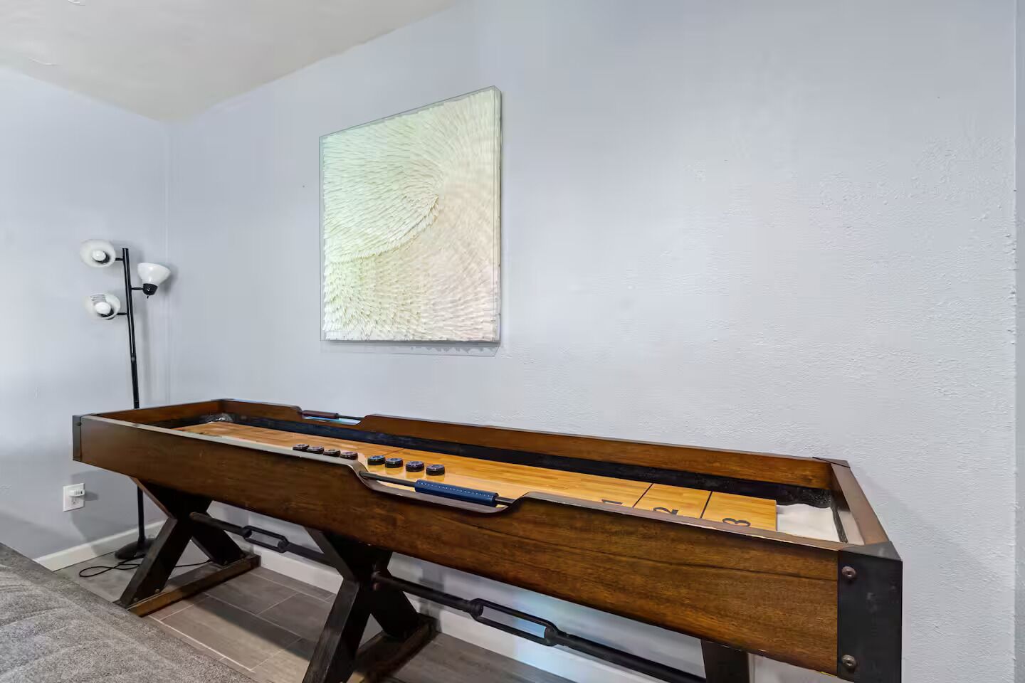 Een tafelvoetbaltafel in een kamer met lichtgrijze muren, een modern abstract schilderij en een vloerlamp.