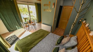 A bedroom with a bed, pillows, a wooden headboard, a radiator, a dining table with chairs, and a view of the outdoors through a window. - Casa Upupa  (Montreuil)