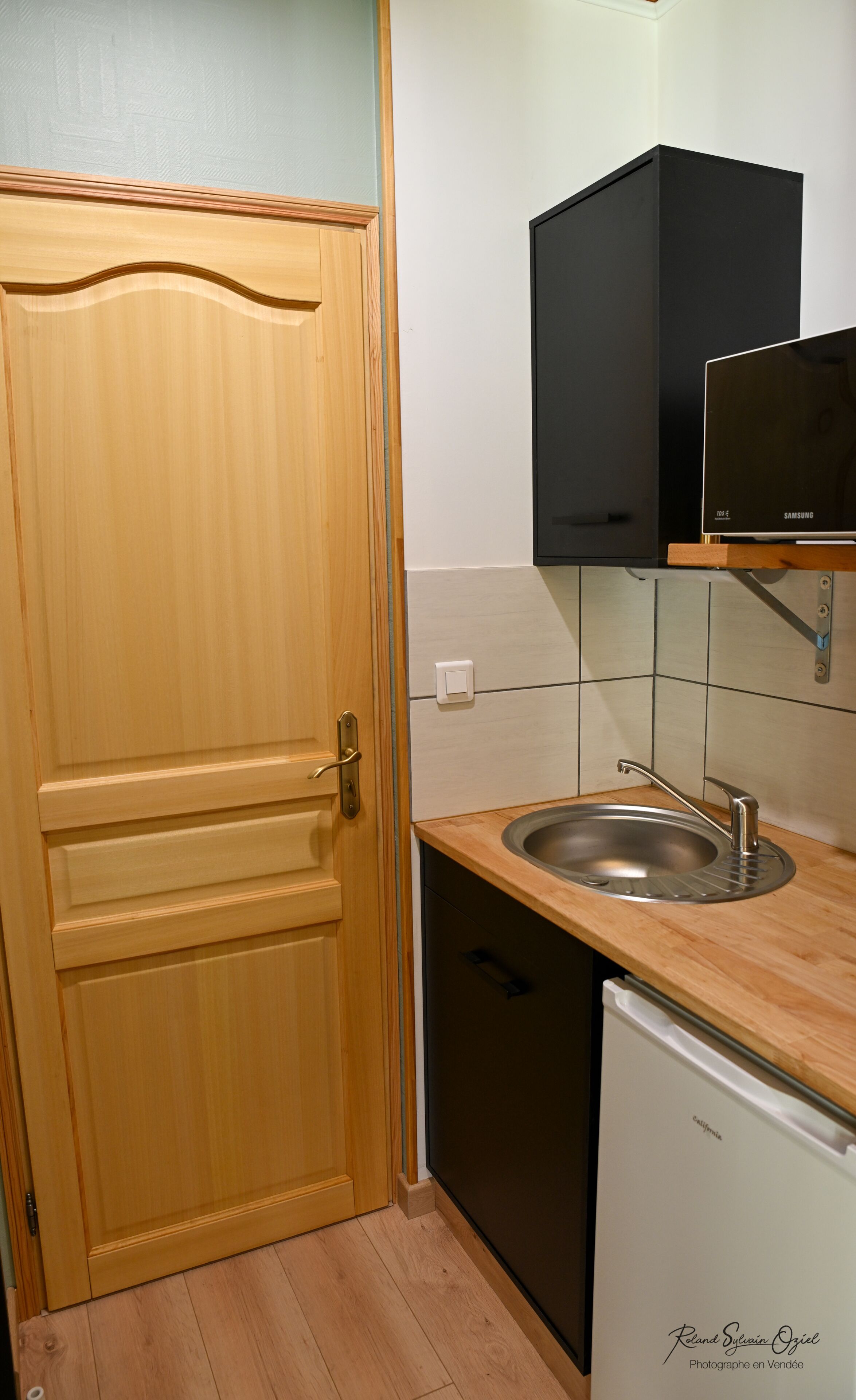 Een keuken met een houten deur, een zwarte magnetron, een spoelbak en een vaatwasser.