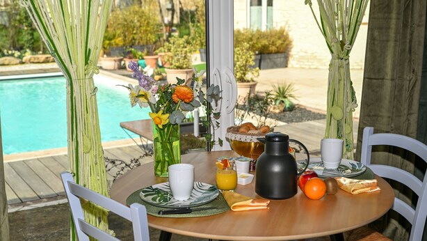 A dining table set outdoors with a view of a swimming pool, surrounded by white chairs and a vase of flowers. - Casa Upupa  (Montreuil)