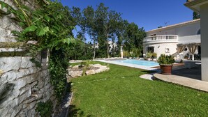 A swimming pool surrounded by a well-maintained lawn, stone walls, and a building with a balcony. - Casa Upupa  (Montreuil)