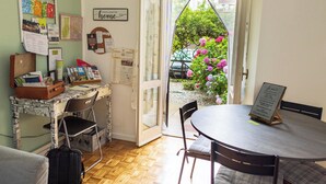 Una habitación con escritorio, silla y mesa, una maleta y vistas a flores a través de una puerta abierta.