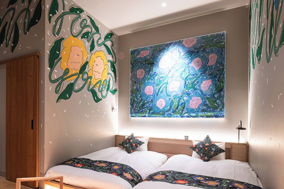 A bedroom with a bed, pillows, a nightstand, and a wall mural.