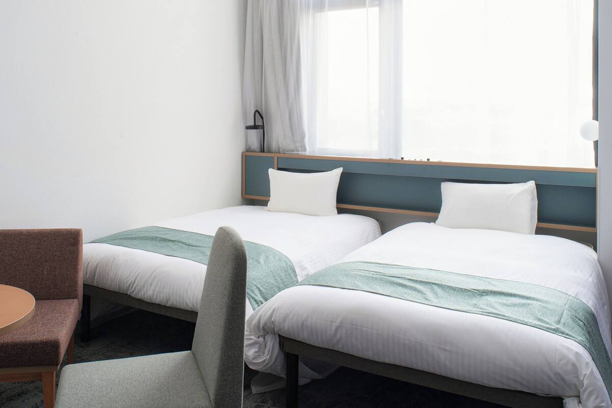 A hotel room with two single beds, a small round table, and a chair.