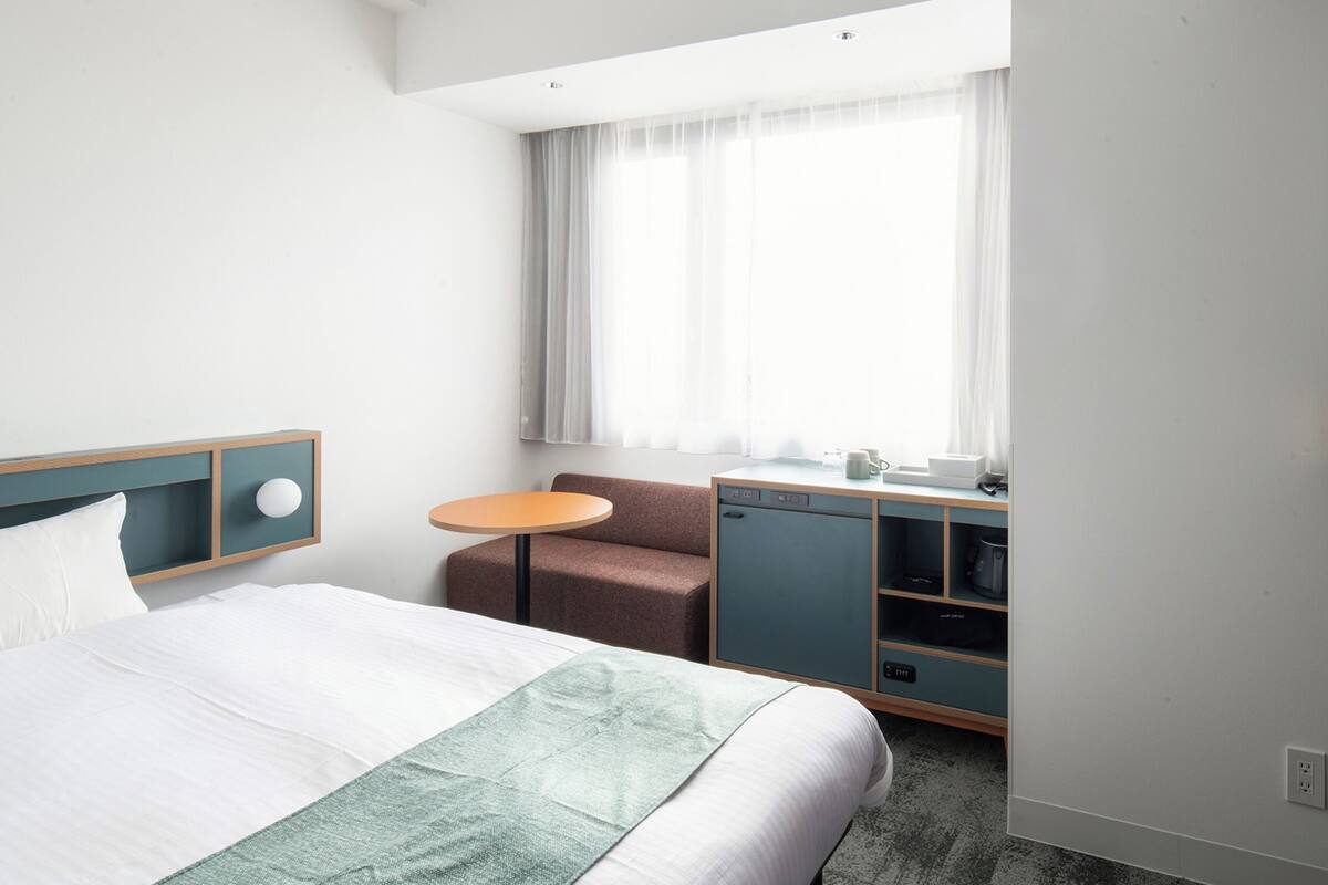 A hotel room with a bed, a desk with a chair, a television, and a window with curtains.