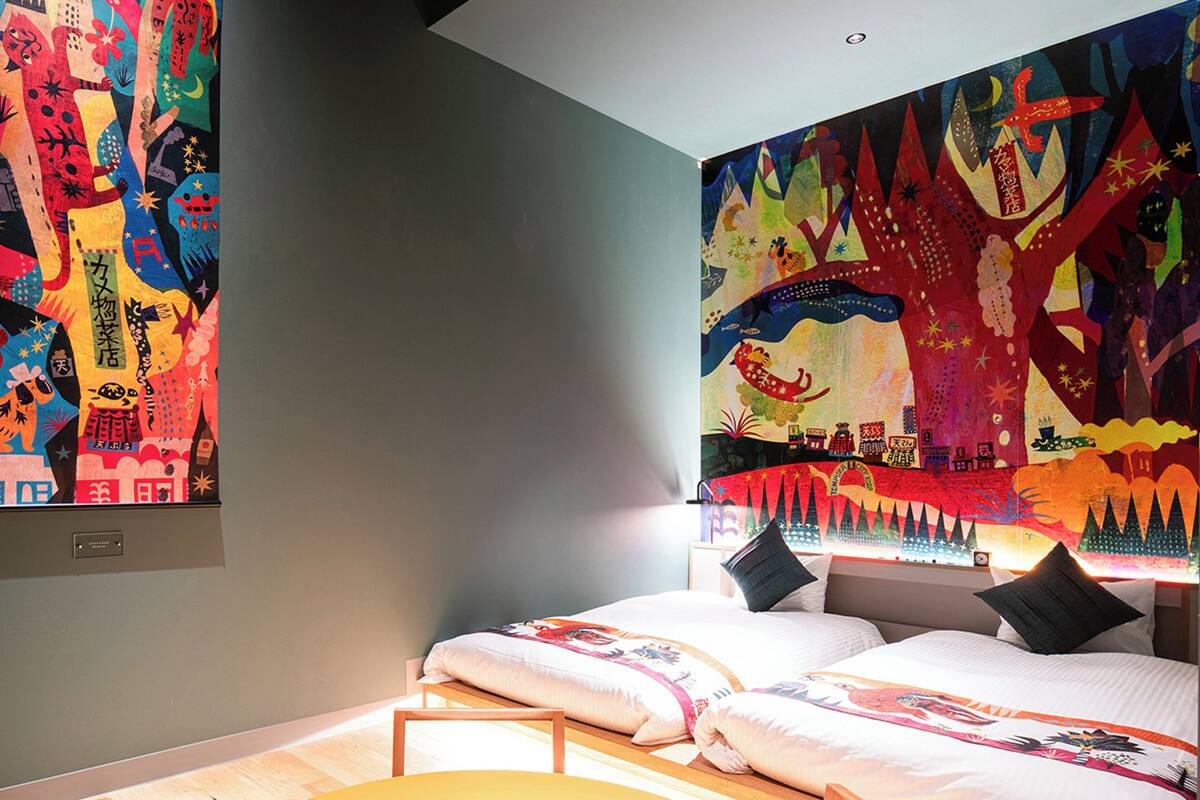 A bedroom with a bed, pillows, and a colorful tapestry on the wall.