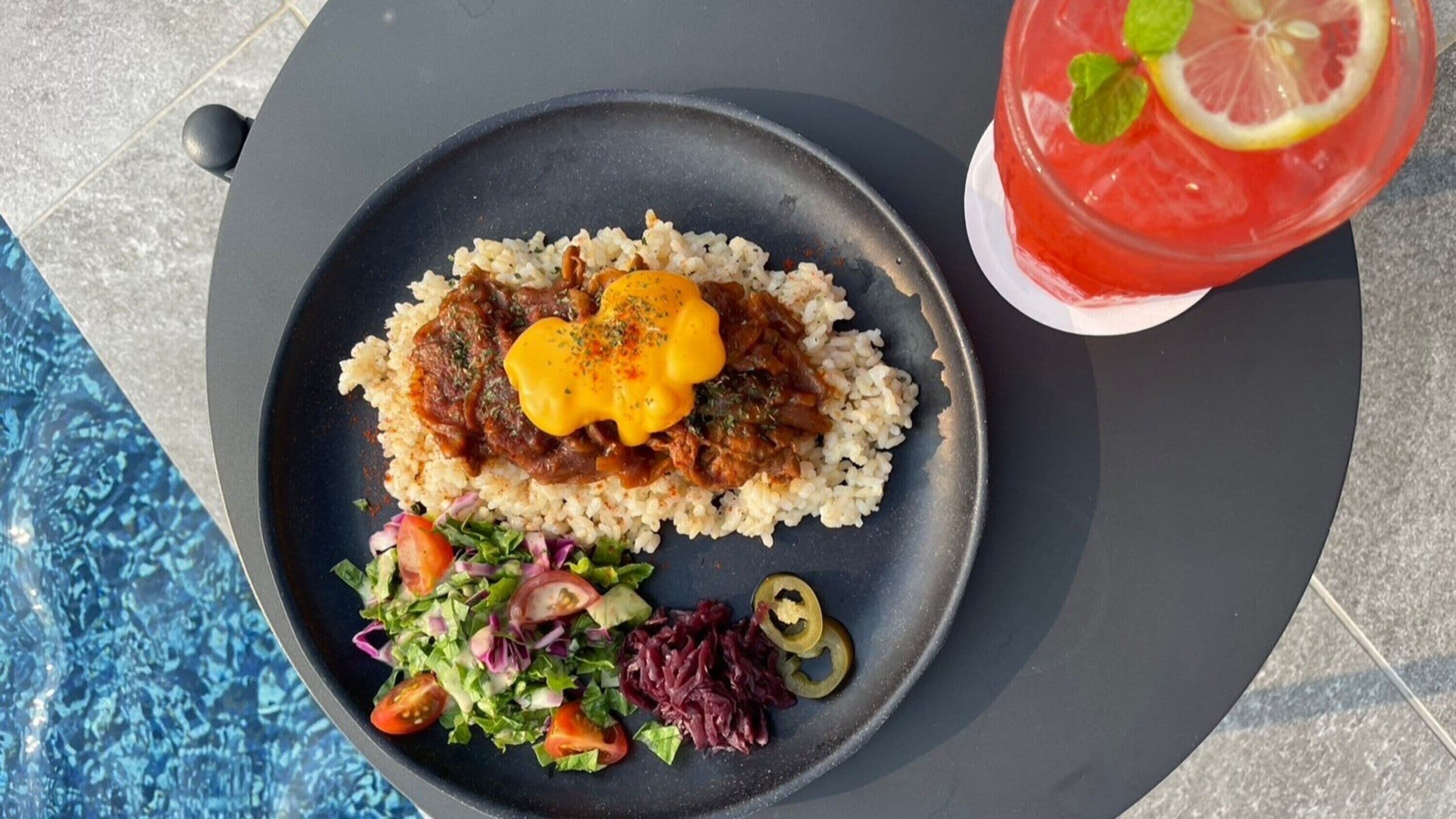 A meal consisting of rice, a meat dish with a yellow sauce, and a side salad with tomatoes and red cabbage.