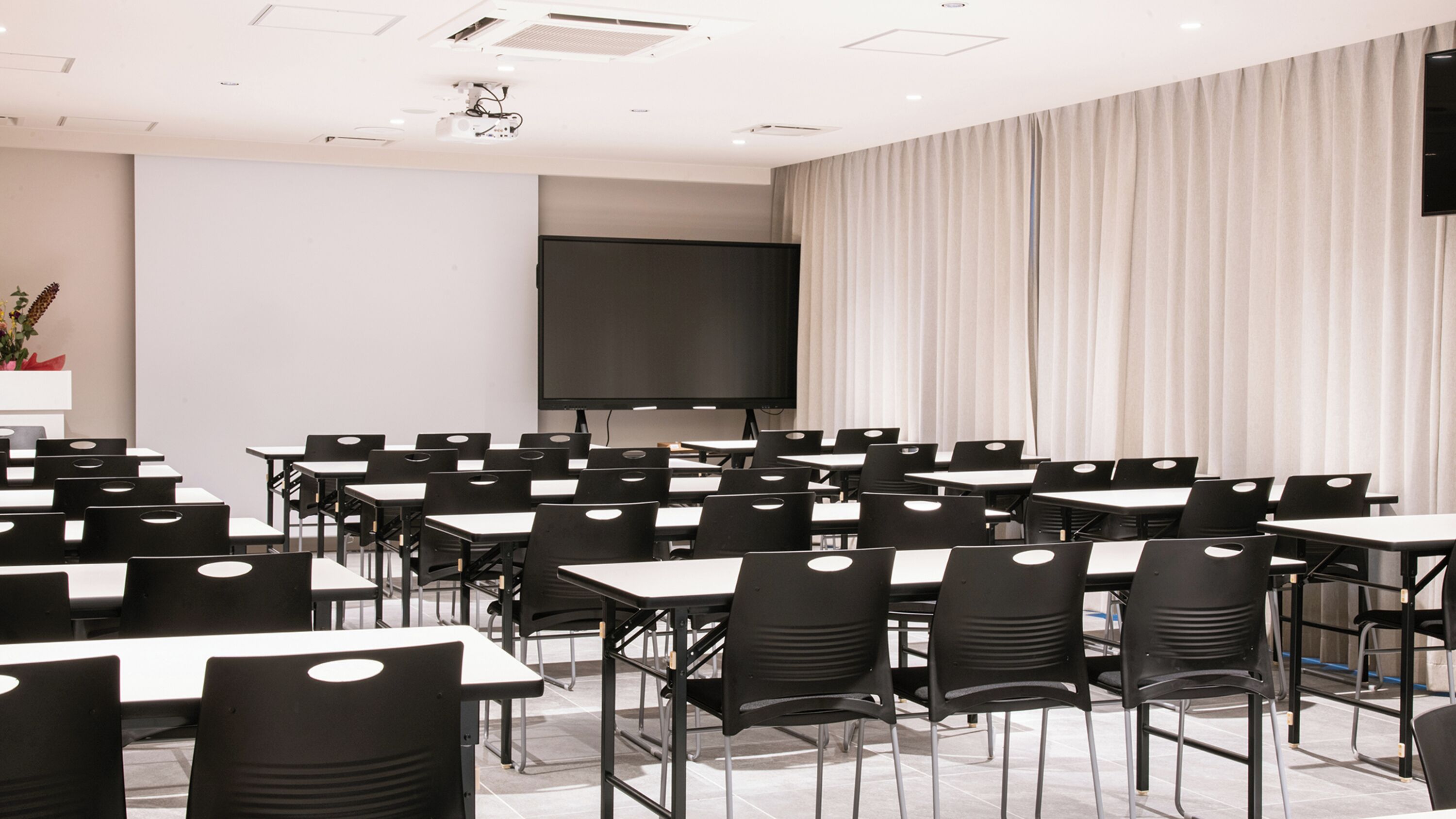 A conference room with multiple tables and chairs, a large screen, and a curtain backdrop.