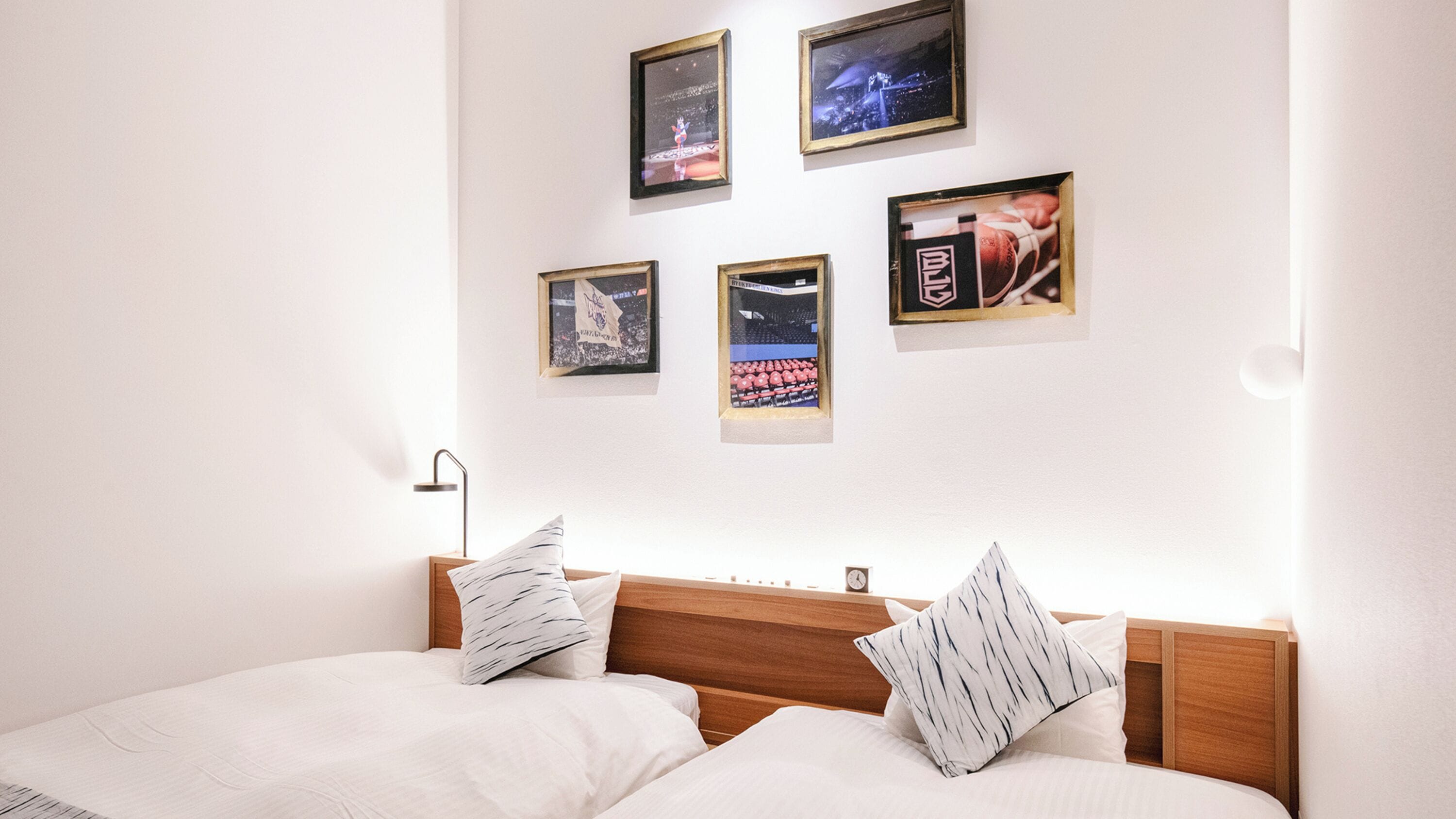 A bedroom with a wooden headboard, two beds with white bedding, and four framed posters on the wall.