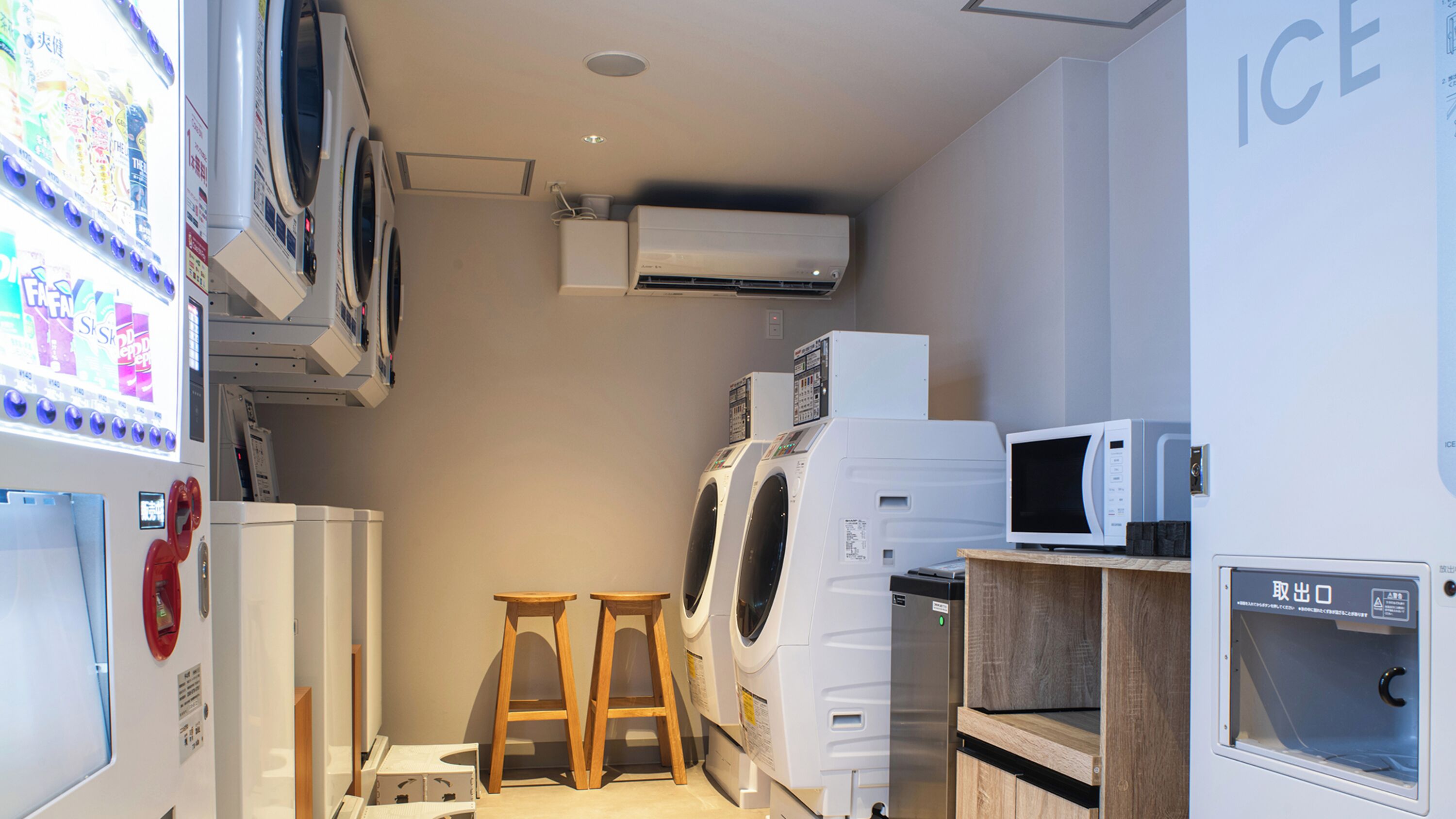 A laundry room with stacked appliances, a wooden stool, and a vending machine.