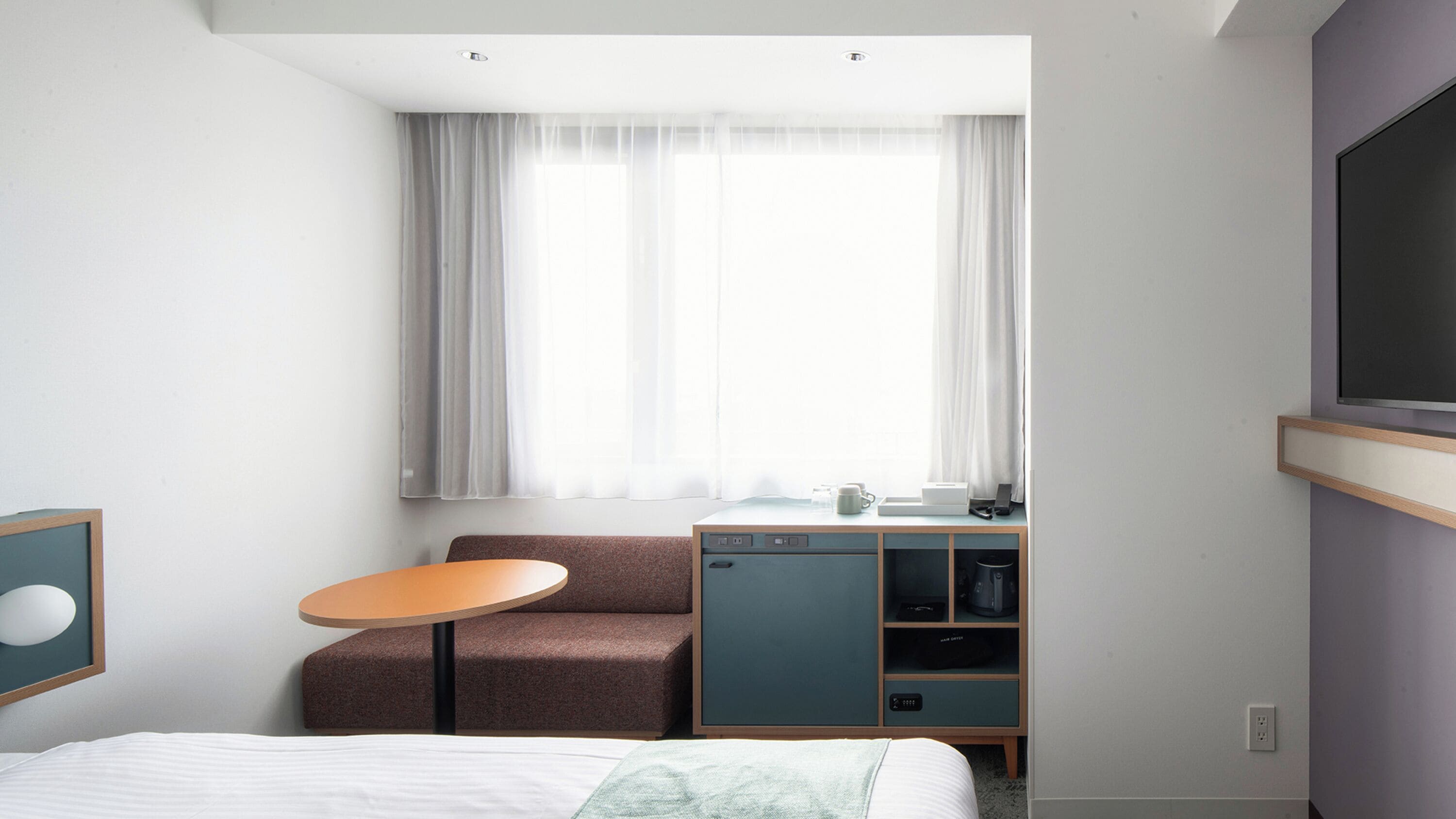 A hotel room with a bed, a small round table, a sofa, a TV, and a window with curtains.