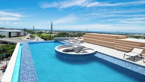 A modern swimming pool with a circular water feature, surrounded by a deck with seating and a view of the ocean. - REF Okinawa Arena by VESSEL HOTELS (Okinawa)