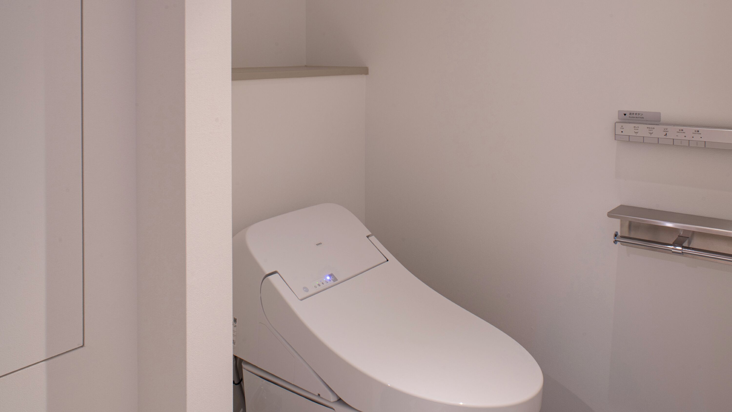 A small, compact bathroom with a toilet, a shelf above the toilet, and a towel rack to the right.