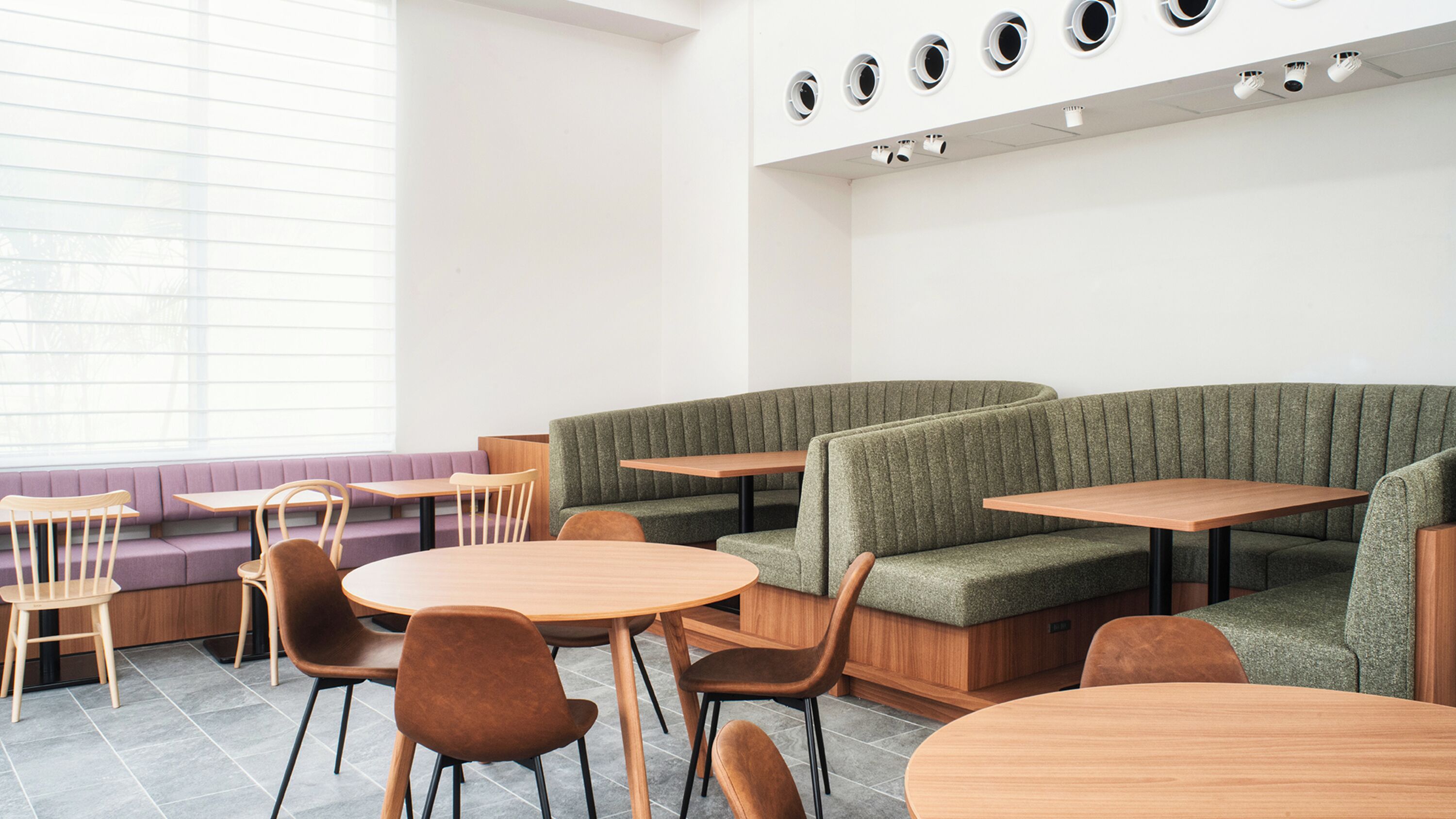 A modern cafe with wooden tables and cushioned seating.