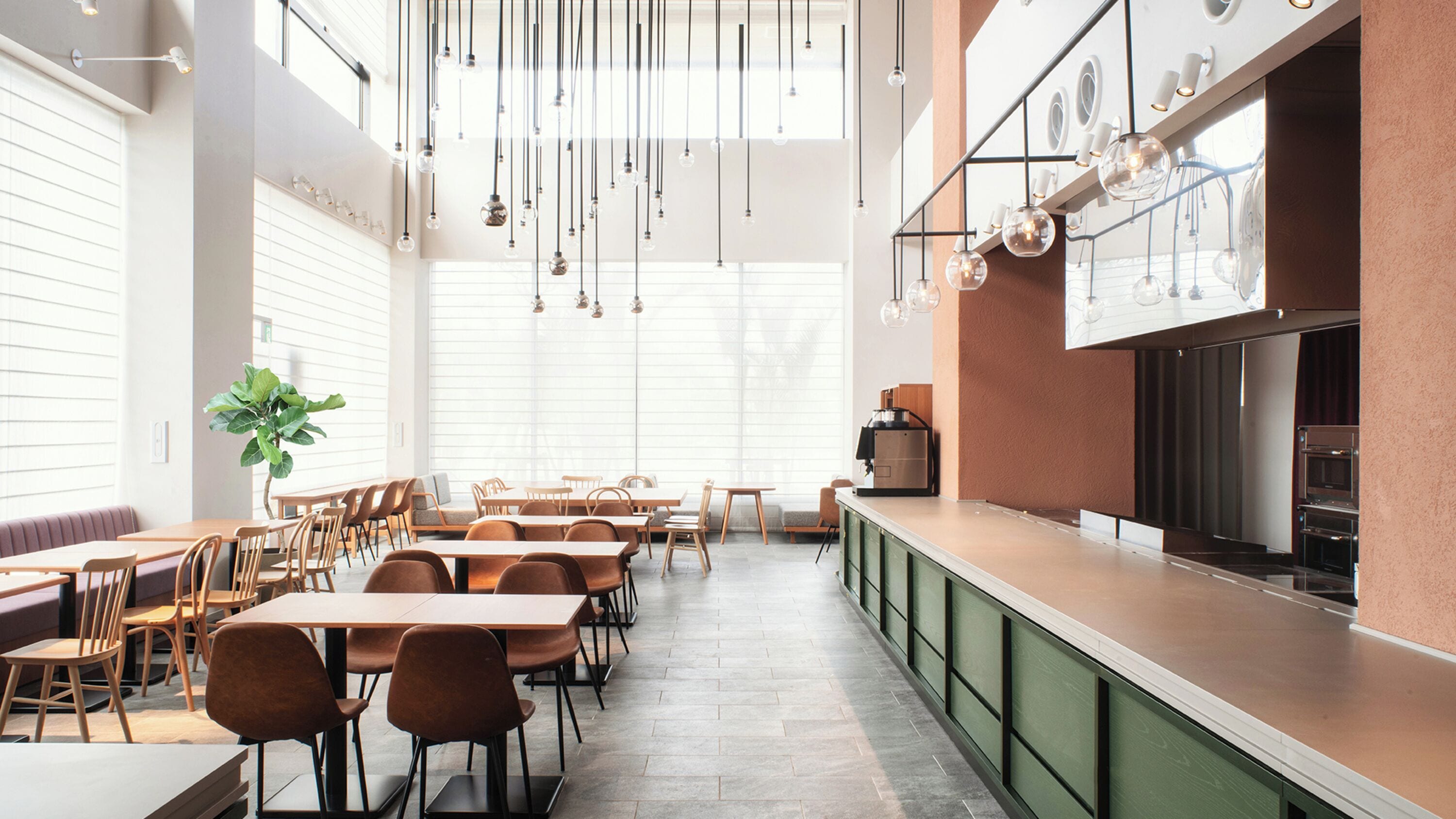 Un restaurante moderno con techos altos, iluminación colgante y una larga barra con zona de cocina a la vista.