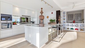 A modern kitchen with white cabinetry, a central island, stainless steel appliances, and a decorative vase. - Villa Panorama Summit (Koh Samui)