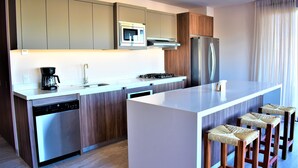Une cuisine moderne dotée d’un îlot central, d’appareils électroménagers intégrés et de tabourets de bar en bois.