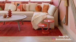 Un salon moderne avec un canapé beige, des coussins rouges et blancs, une table basse ronde et un tapis rouge.