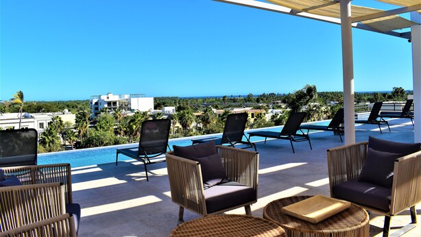 Un espace aménagé au bord de la piscine, avec des meubles en osier, une vue sur l’océan et un ciel d’un bleu limpide.
