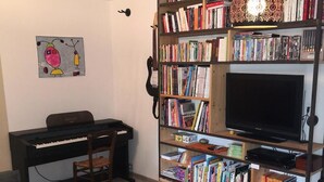 A living room with a sofa, a coffee table, a desk with a computer, a bookshelf filled with books, a television, and a hanging light fixture. - Pretty house Aix en provence / Fuveau (Fuveau)