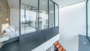 A modern hotel room with a large glass wall, a wooden staircase, and a view of the outdoors. - Loft Alex (Canggu)