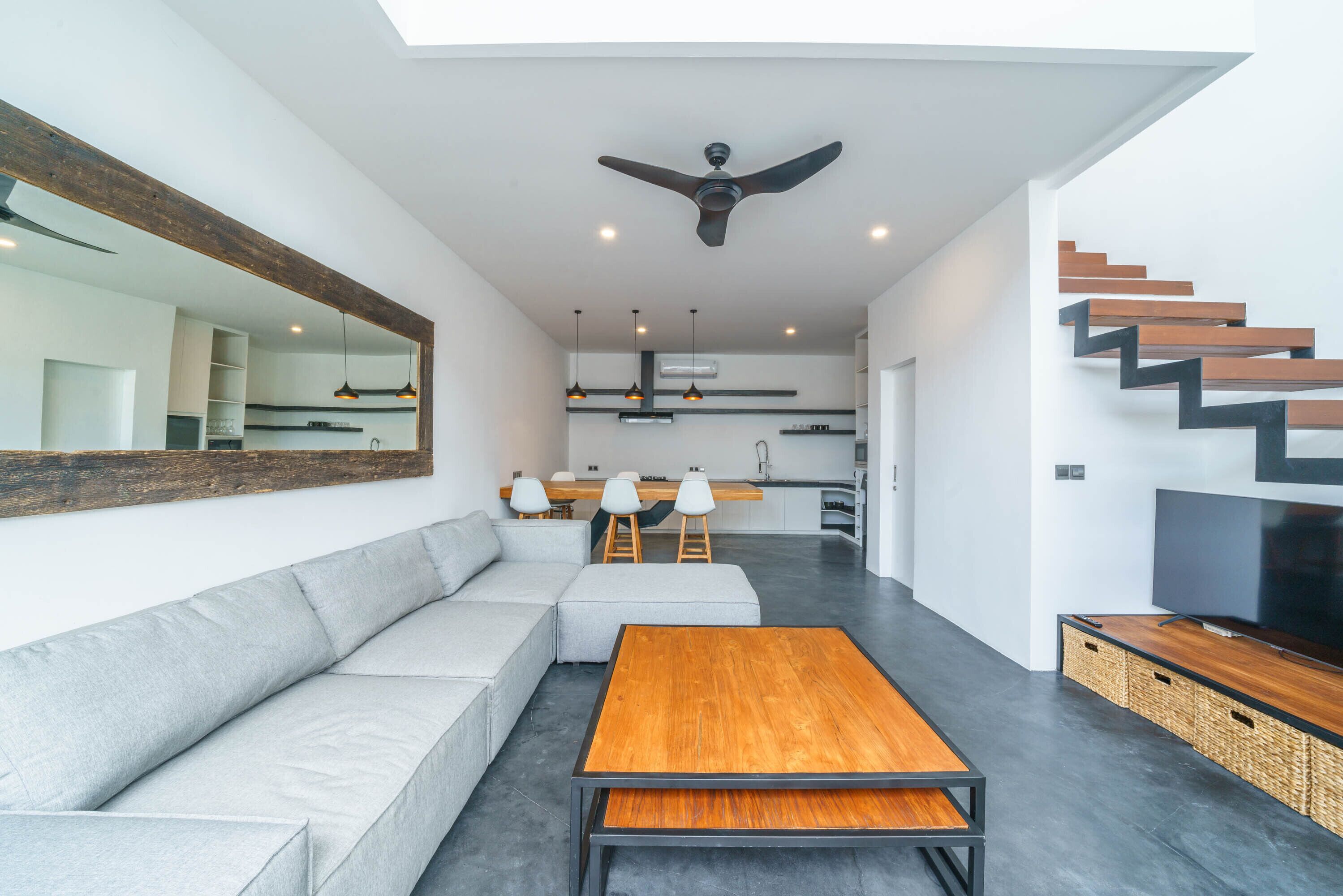 A modern living room with a sofa, a wooden coffee table, a TV, and a staircase.