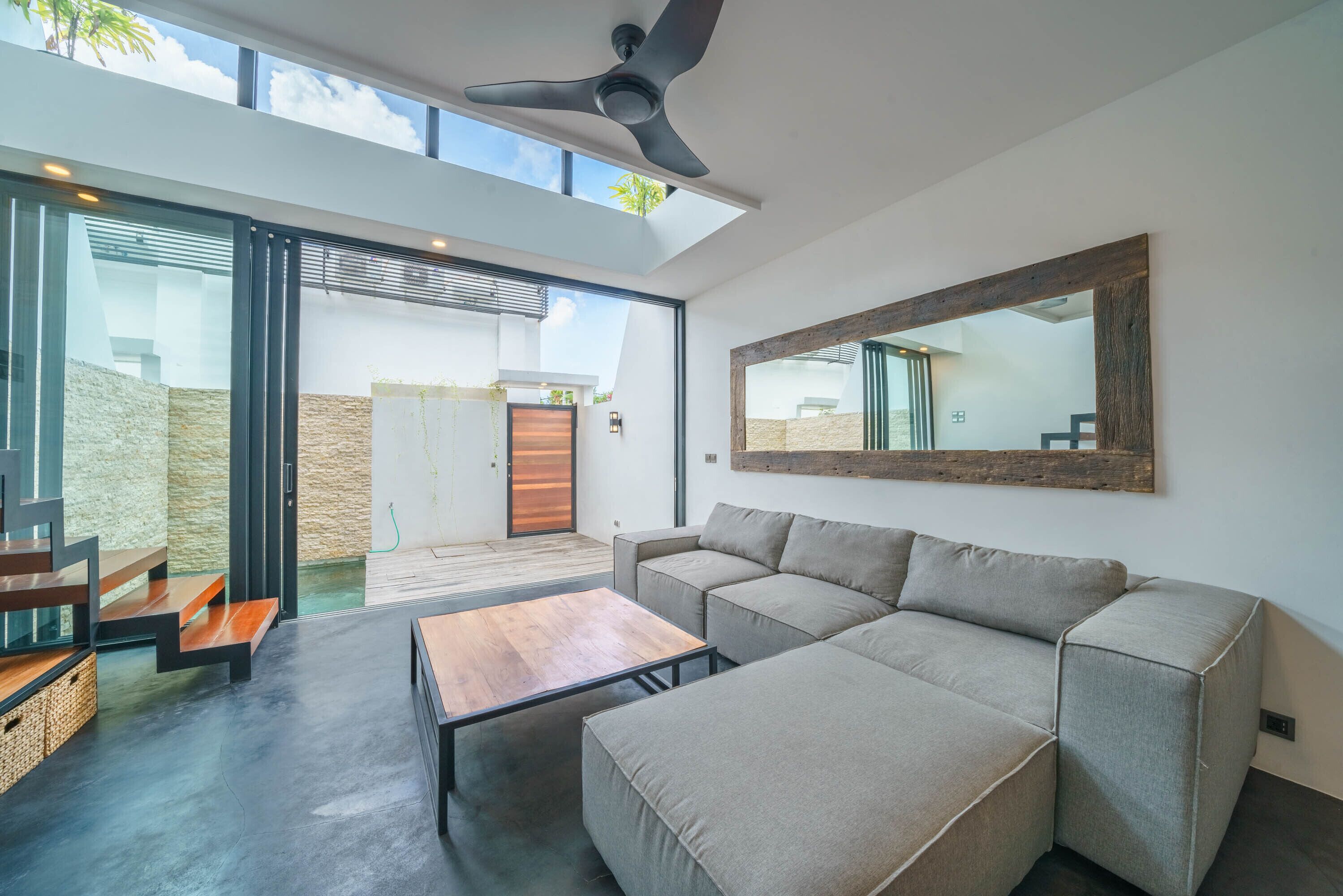 Una sala de estar moderna con un sofá modular, una mesa de centro de madera y un ventilador de techo.