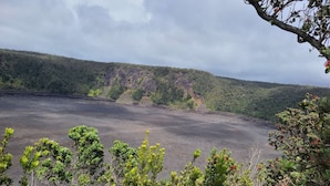 Paisaje volcánico con un campo de lava y colinas boscosas al fondo.