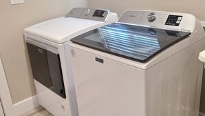A laundry room with a front-loading washer and dryer, a window with blinds, and a light switch on the wall. - Air Conditioned 2 Bedrooms 1 Bath Apartment, fine decorated, Free Laundry in HPP (Keaau)