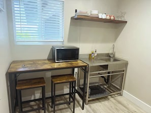 Una kitchenette compacta con microondas, lavamanos y taburetes de bar.