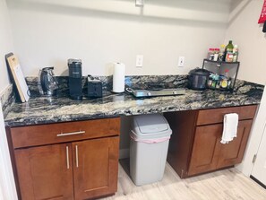 Eine Küche mit einer Granitabdeckung, einer Kaffeemaschine, einem Toaster, einem Mülleimer und einem Regal mit Gewürzen.