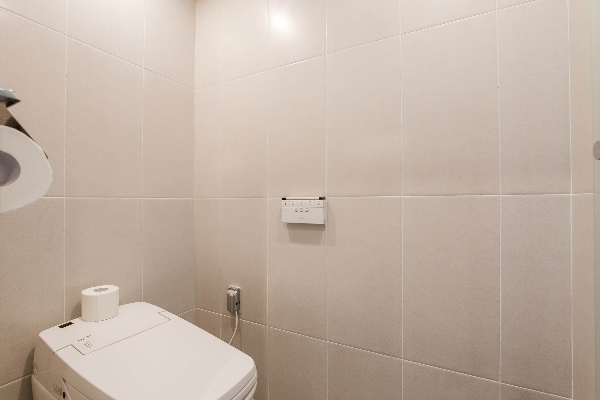 A bathroom with a toilet, a paper towel dispenser, and a wall-mounted electrical outlet.