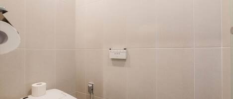 A bathroom with a toilet, a paper towel dispenser, and a wall-mounted electrical outlet.