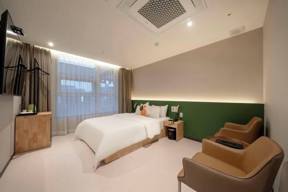 Habitación de hotel con cama, escritorio, silla, televisor y ventana con cortinas.