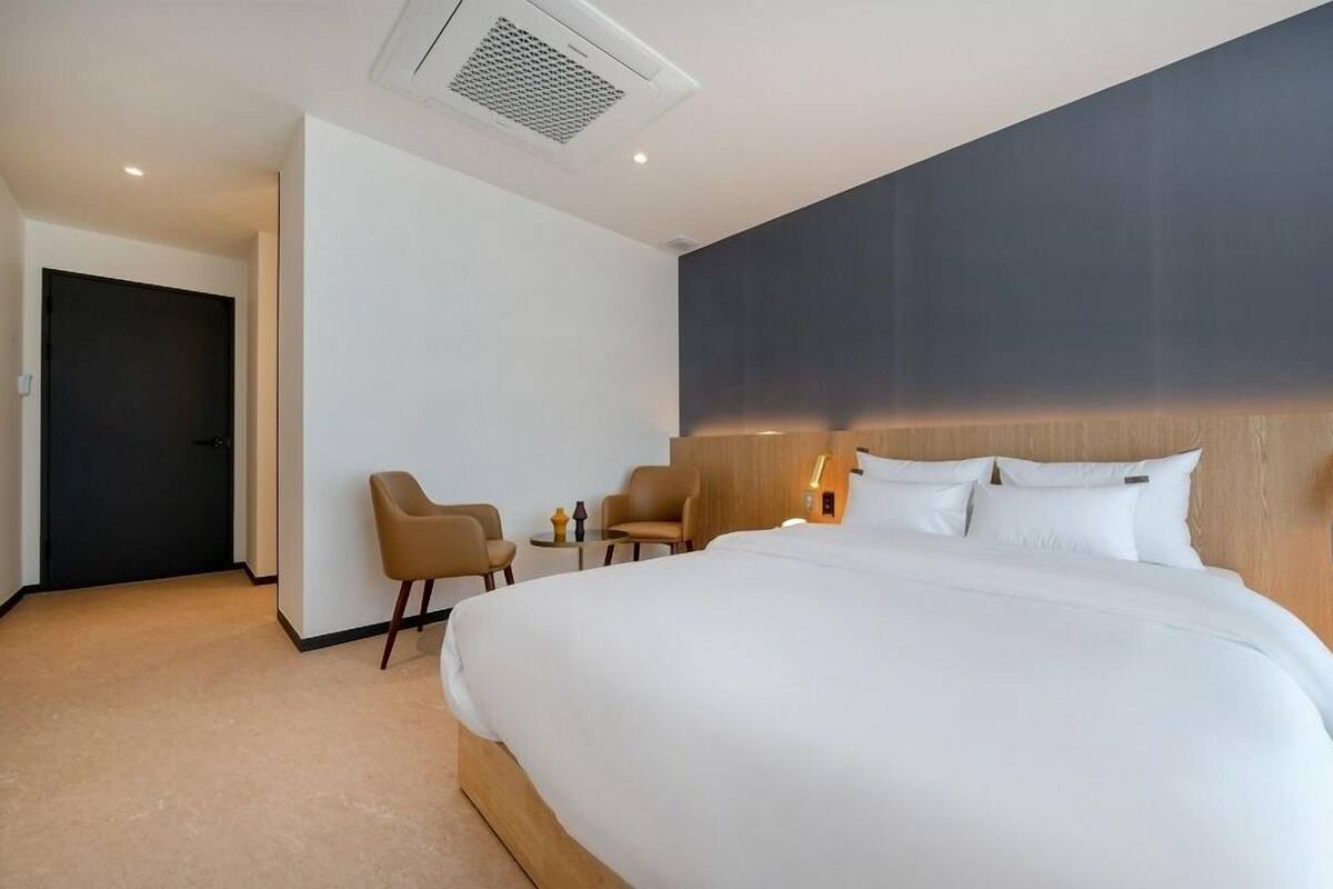 Habitación de hotel con una cama grande, dos sillones, una mesita y una pared de color oscuro.