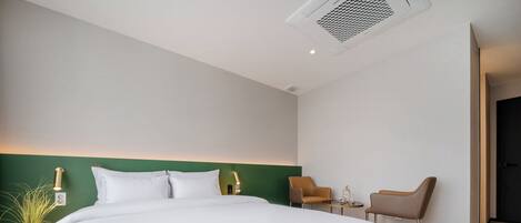 Una habitación de hotel moderna con una cama grande, dos sillones, una mesita y una pared de acento verde.