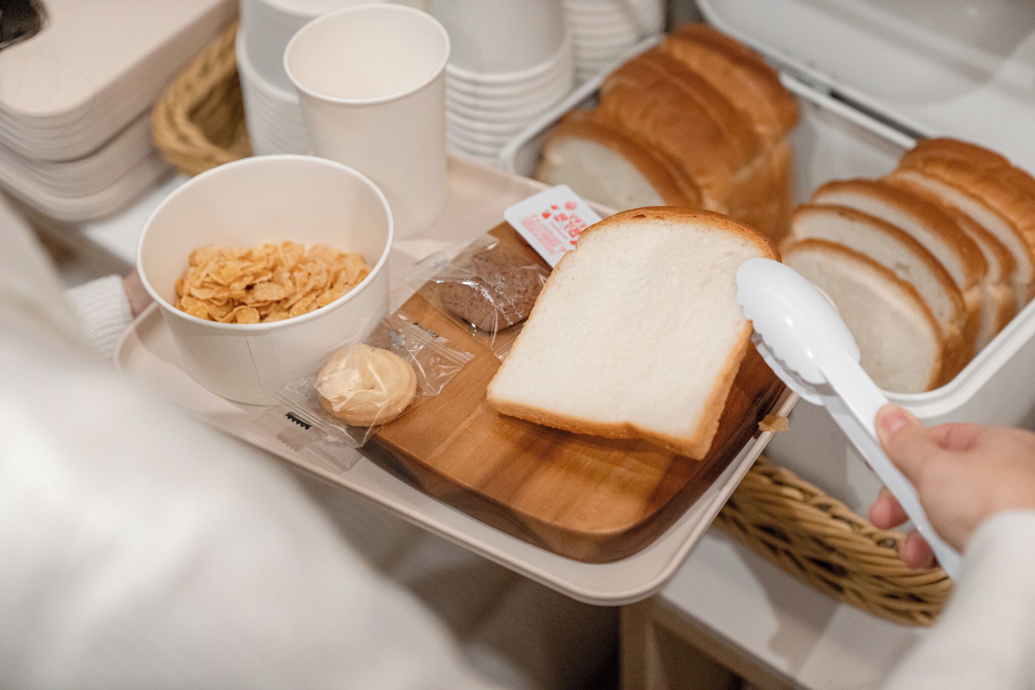 A tray with sliced bread, a bowl of cereal, and a container of butter.