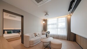 Una habitación de hotel moderna con cama, sofá, reposapiés y un ventanal con cortinas.